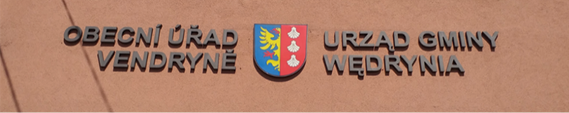 Dwa zdjęcia obok siebie. Na pierwszym zdjęciu znajduje się fragment elewacji domu, na którym są przymocowane poszczególne litery nazwy urzędu gminy. Wlewo jest czeska nazwa „Obecní úřad Vendryně”, wprawo znajduje się „Urząd gminy Wendrynia”. Pomiędzy widnieje znak gminy. Czeski i polski napis są formalnie identyczne. Także drugie zdjęcie przedstawia fragment elewacji domu i zainstalowaną na nim białą, metalową tablicę w kształcie prostokątu. Niebieską czcionką w środku tablicy zapisano „Školní družina / Świetlica szkolna”. U góry są dwa mniejsze napisy – „Základní škola s polským jazykem vyučovacím / Szkoła podstawowa z polskim językiem nauczania”. Pod spodem widnieje adres placówki – „Český Těšín, Havlíčkova 13, okres Karviná”. Graficznie są dwujęzyczne napisy tożsame.
