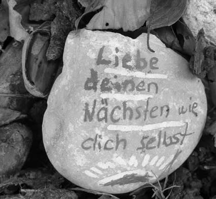 A stone with German text painted on it that reads "Liebe deinen Nächsten wie dich selbst" surrounded by leaves and natural debris.

Description generated by AI