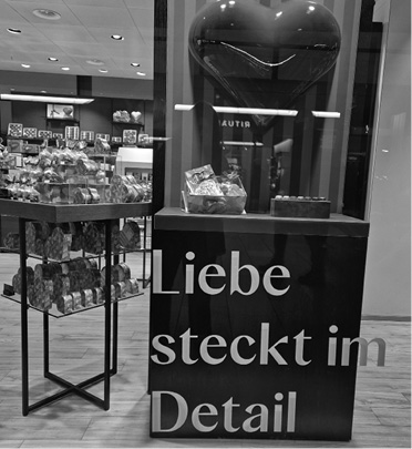 A store display features a large heart-shaped object and a sign with the German phrase Liebe steckt im Detail, surrounded by shelves of packaged goods.

Description generated by AI