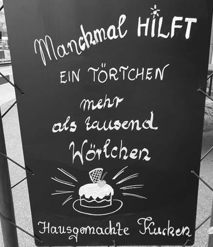 A chalkboard sign with handwritten German text promoting homemade cake with a small drawing of a cake on a plate.
Description generated by AI